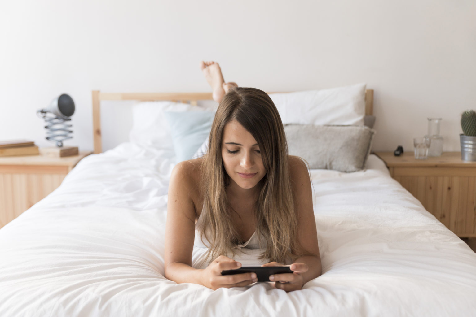 Девојка на кревет со телефон гледа порно за откривање на фантазии